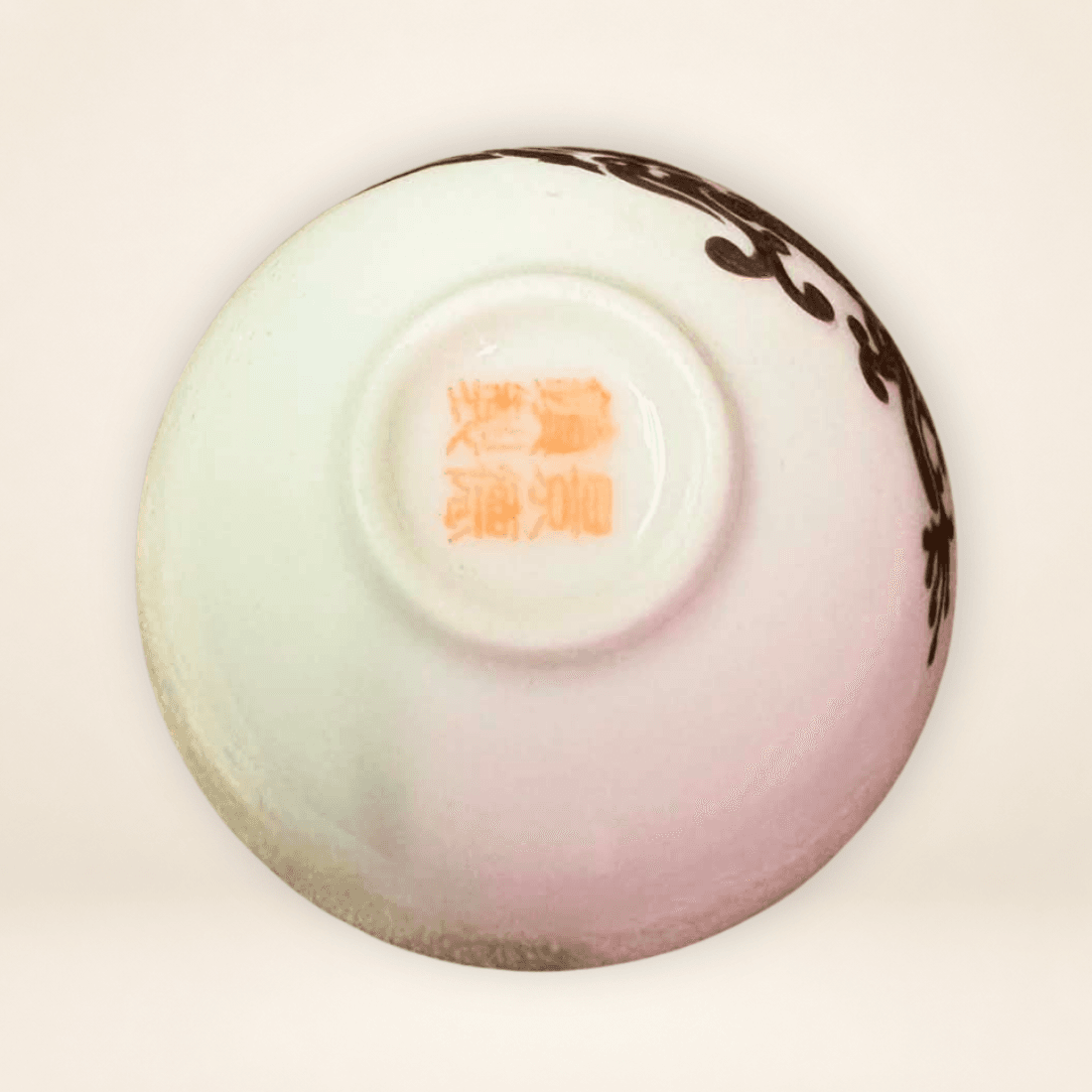 Underside of Chinese tea cup showing orange-red seal-style ceramic mark