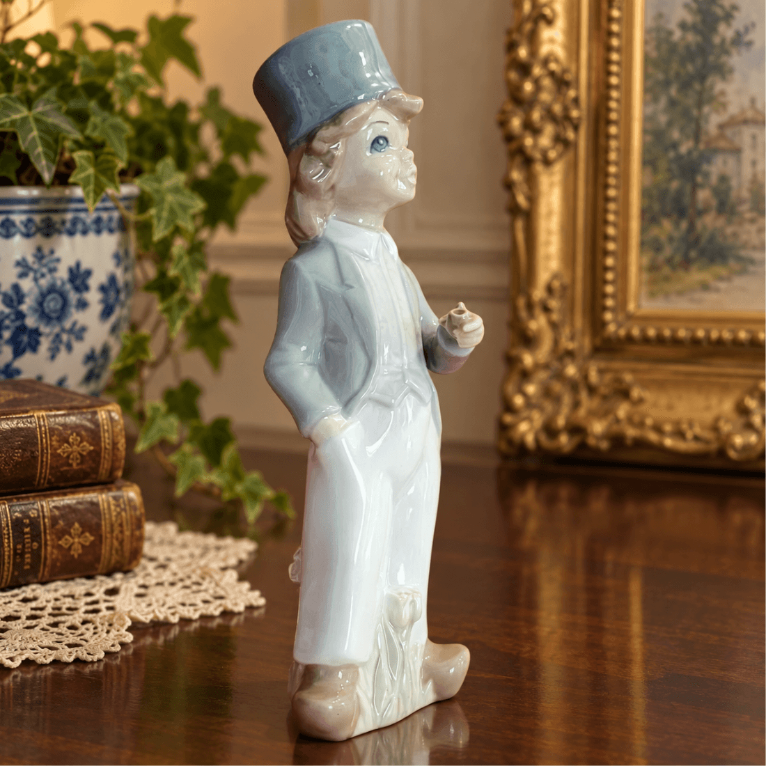 Casades porcelain boy with pipe displayed on a wooden surface beside books and a framed picture