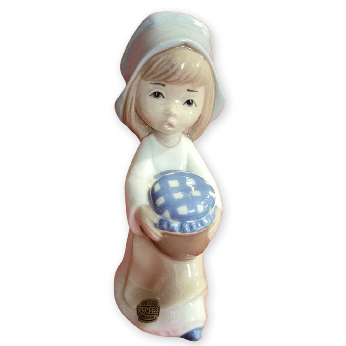 Casades girl figurine facing forwards, wearing a pale blue bonnet and holding a brown jar with a blue-and-white checked covering