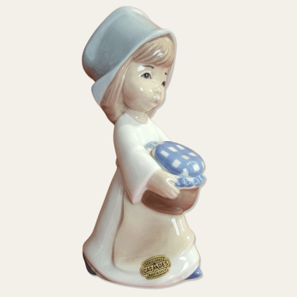 Angled view of the Casades girl figurine showing her blue bonnet, hands around the brown jar and checked jar covering