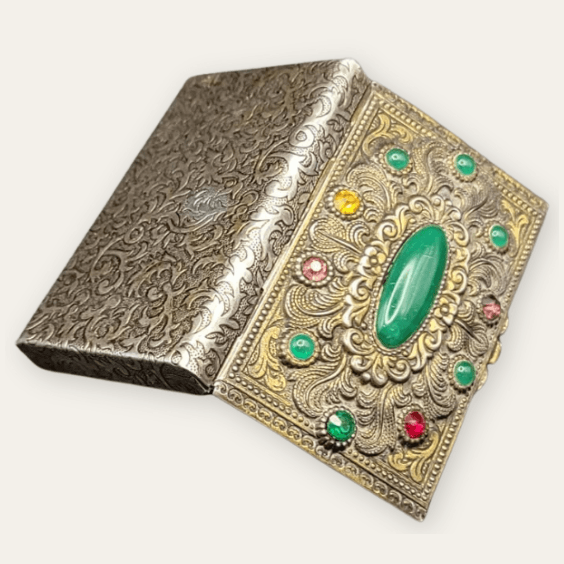 Angled view of the decorated metal box showing its green cabochon lid and patterned underside